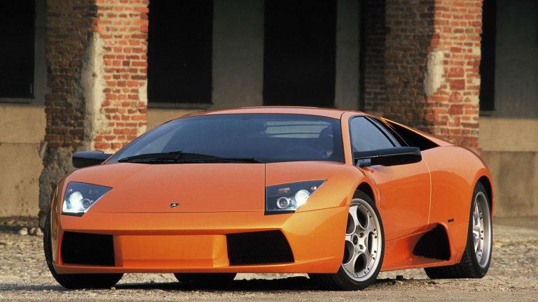an orange sports car parked in front of a brick building.