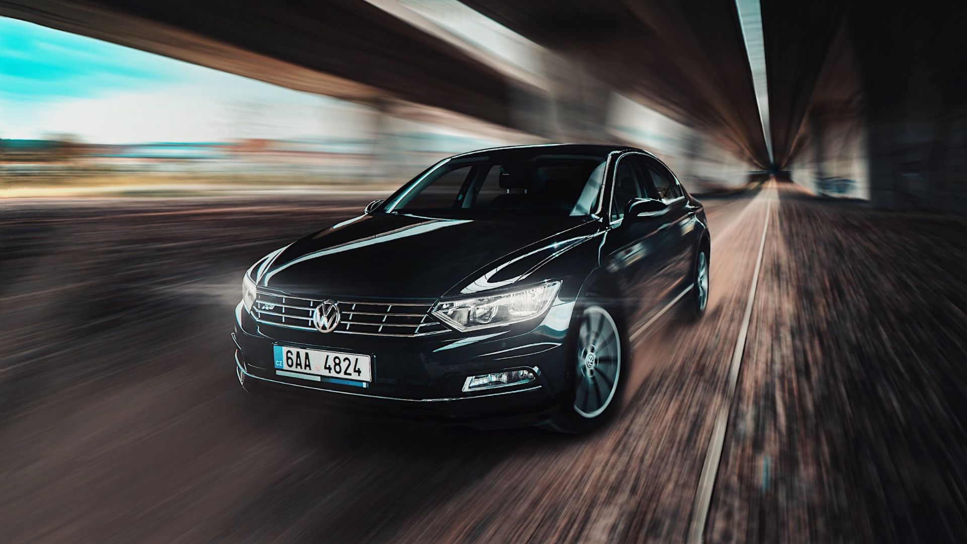 a black car driving down a road next to a tunnel.