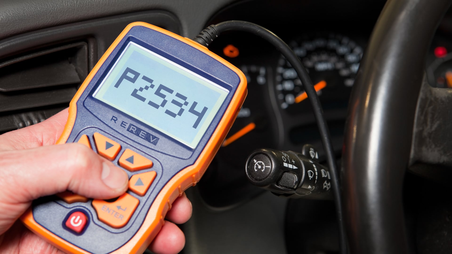 A person holding a tire pressure gauge in a car.