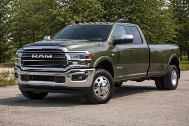 A green Ram 3500 pickup truck with dual rear wheels is parked on a paved surface, surrounded by trees and grass in the background.