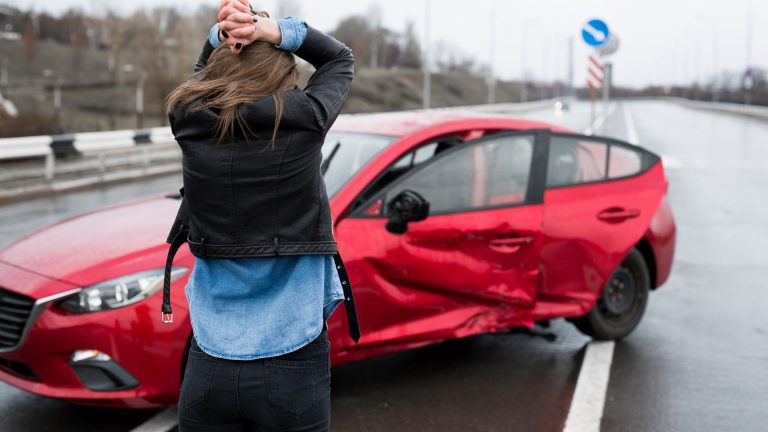 a woman standing next to a red car on a wet road.