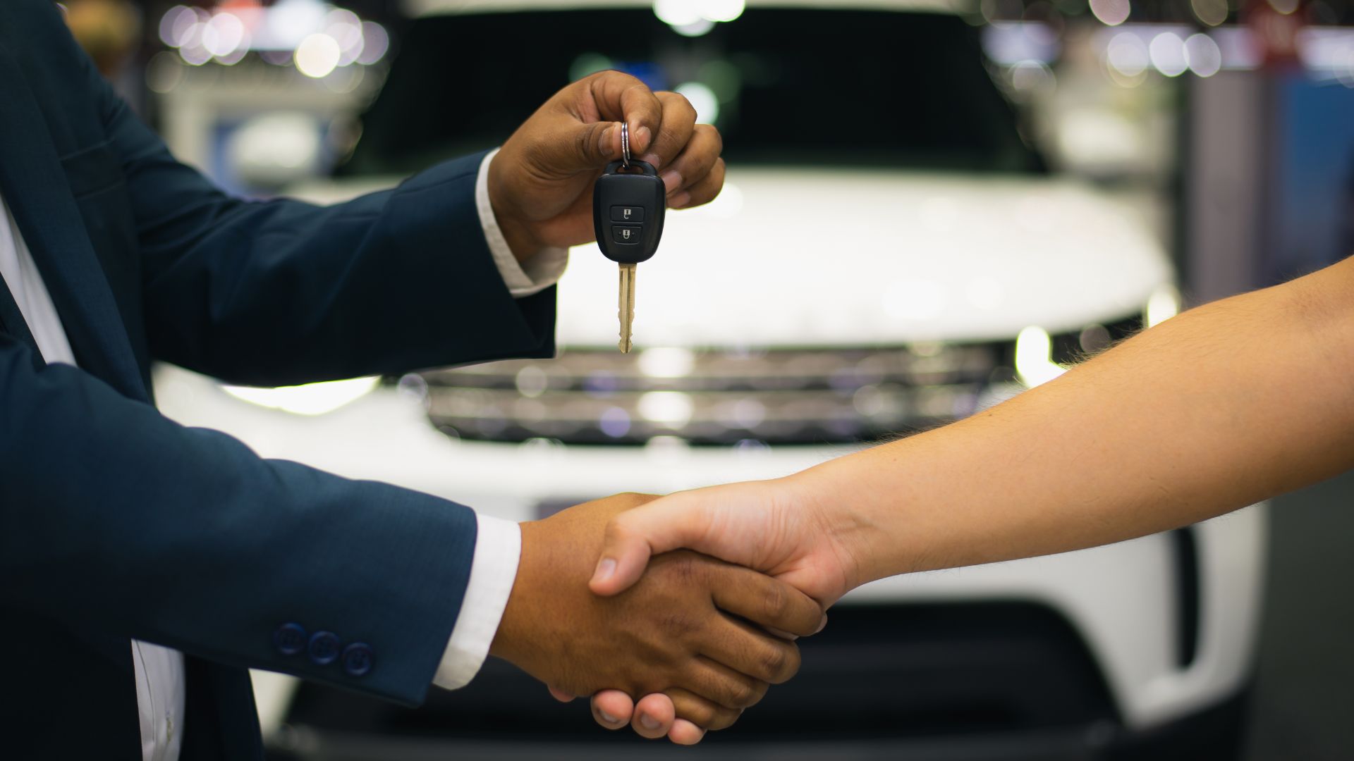 a couple of people shaking hands in front of a car.