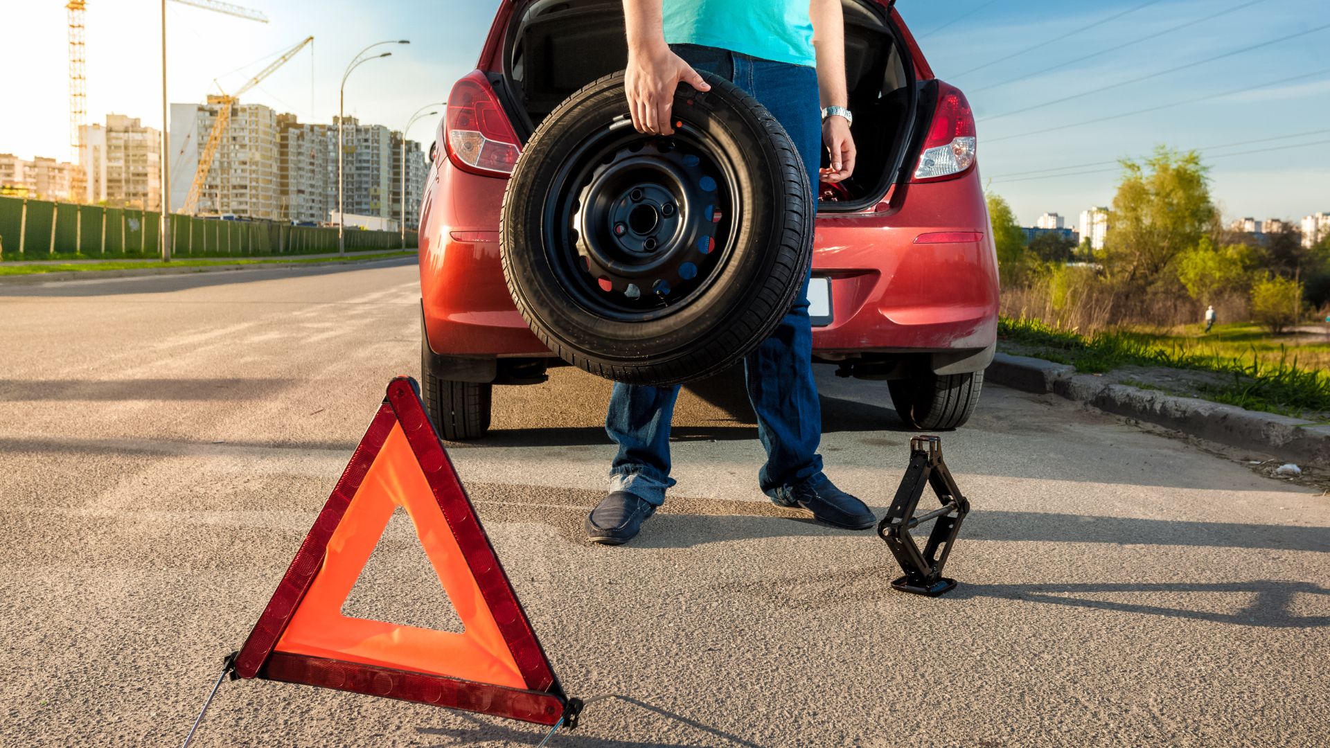 a man standing next to a car holding a tire.