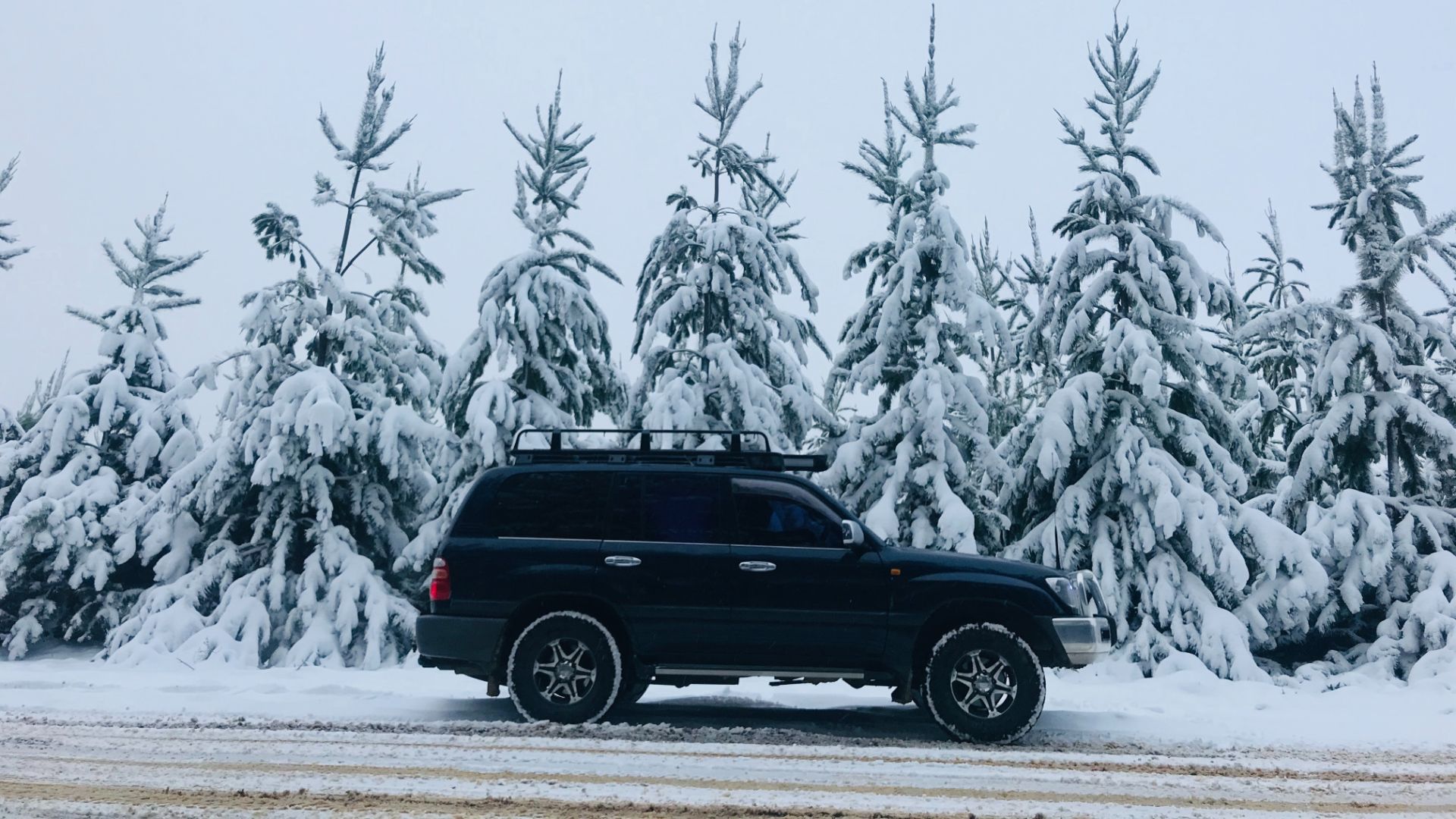 a black truck driving down a snow covered road.