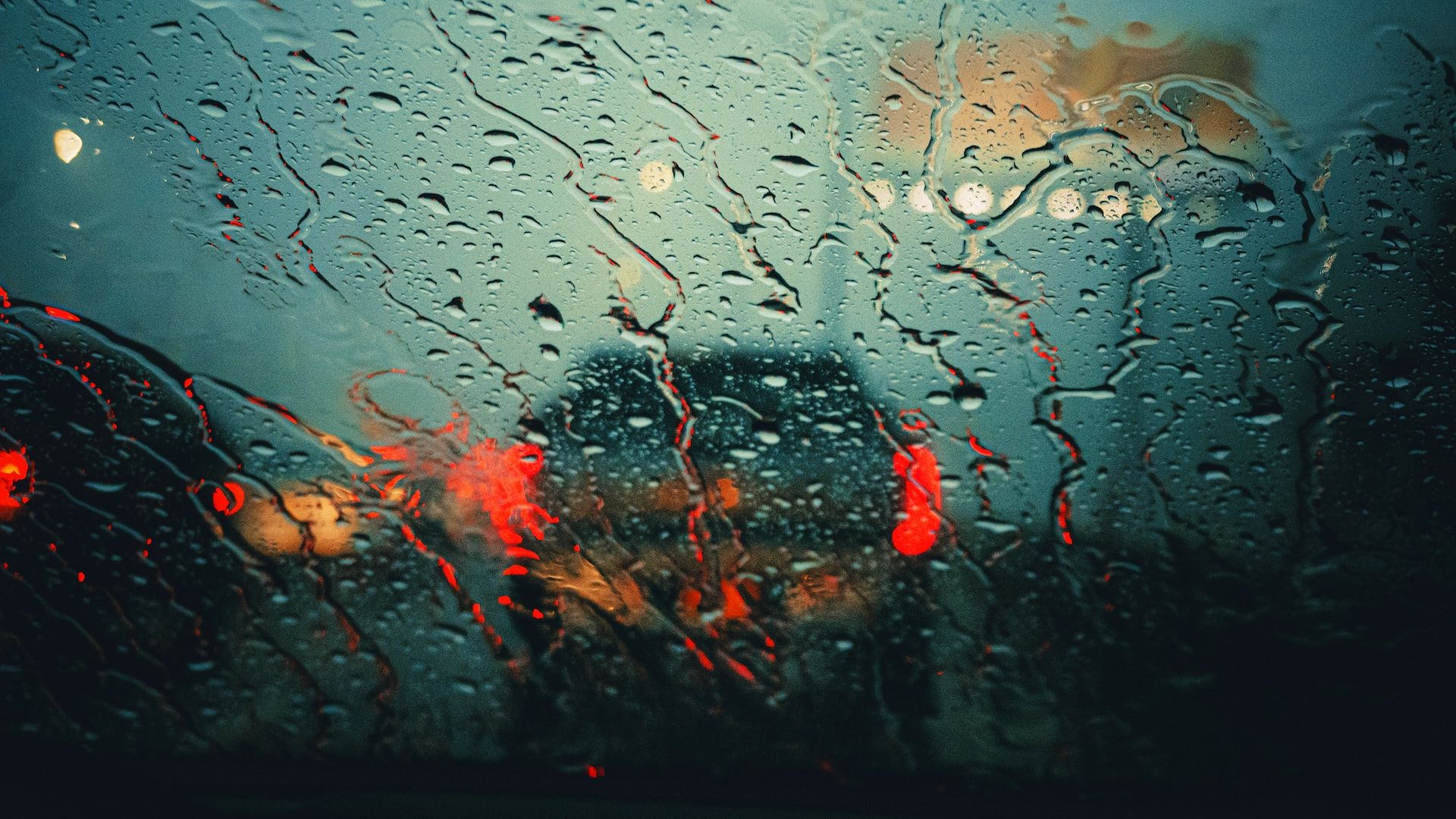 a rain covered window with red lights in the background.