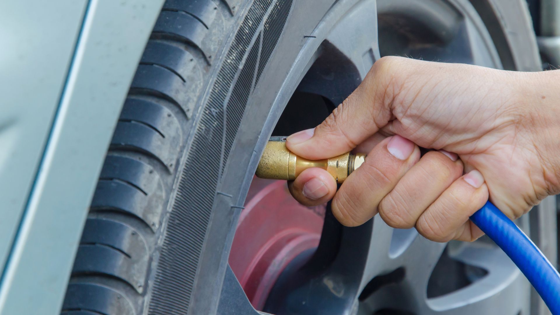 a person holding a hose to a car tire.