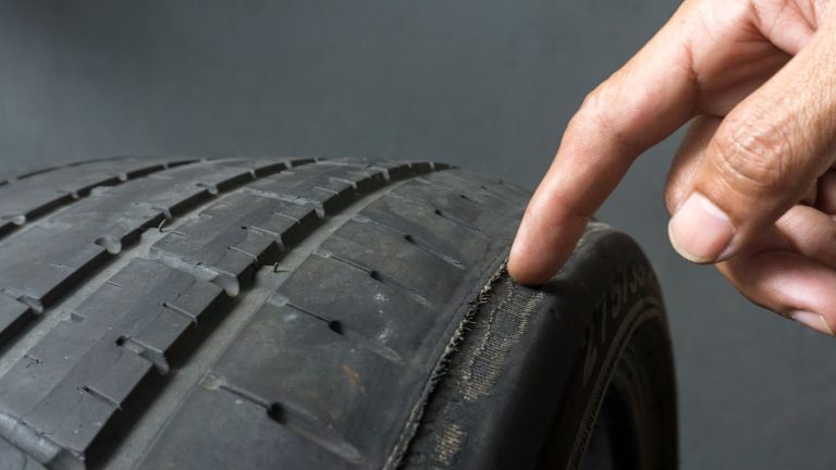 a hand pointing at a tire on a gray background.