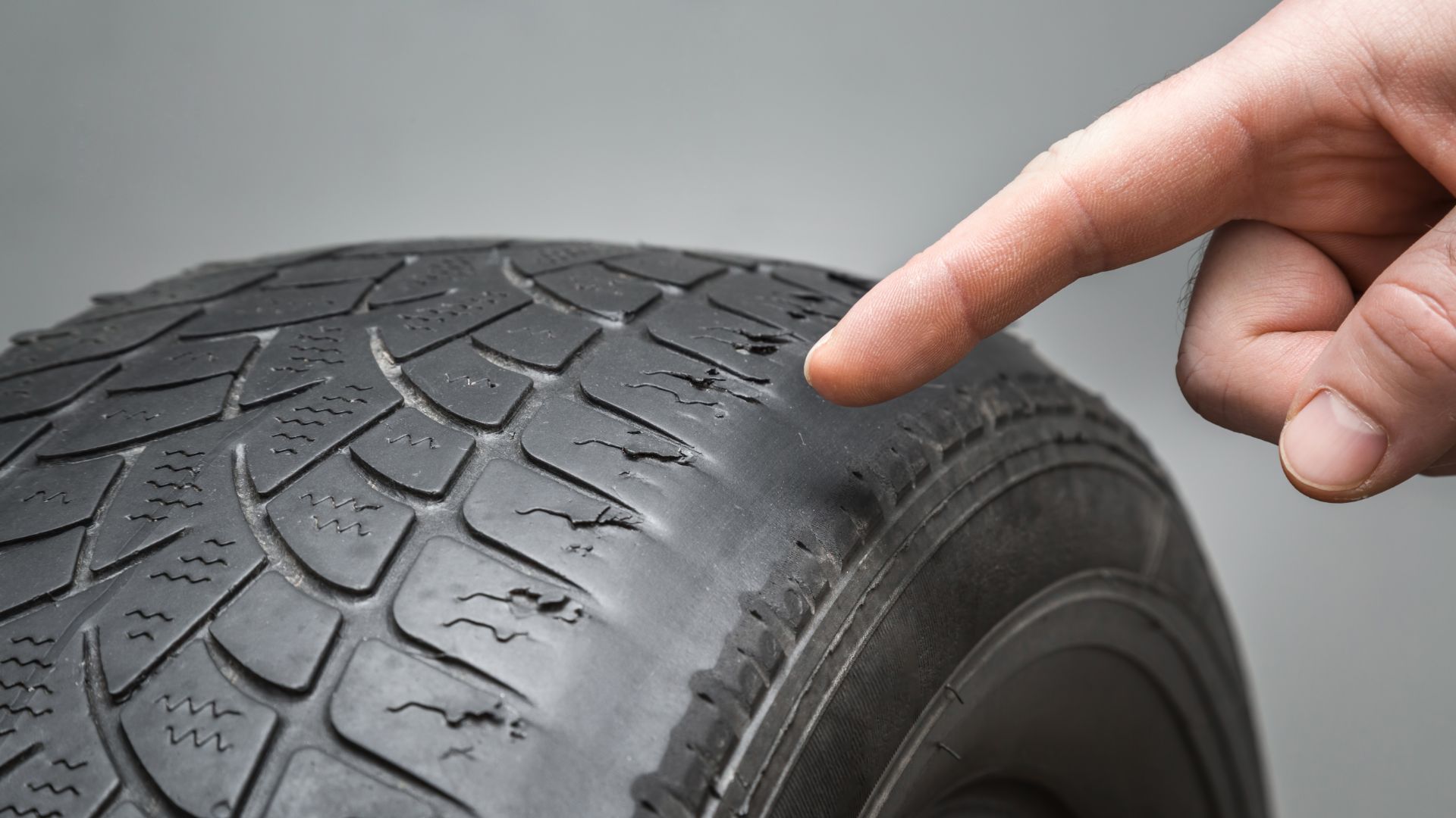 a hand pointing at a tire on a gray background.