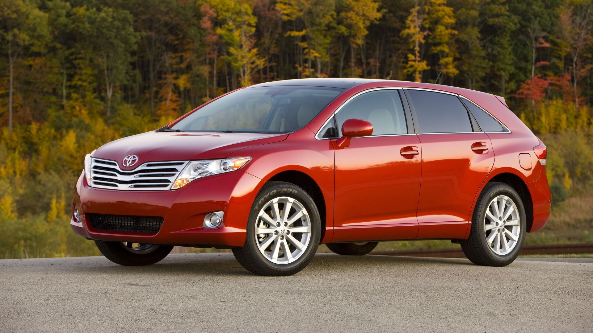 a red toyota venza parked in front of a forest.