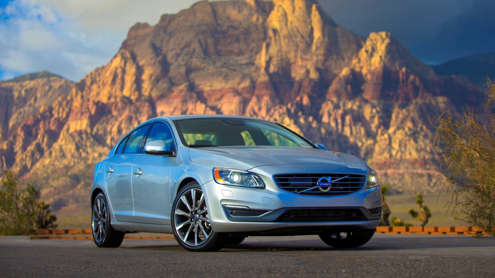 a silver volvo car parked in front of a mountain.