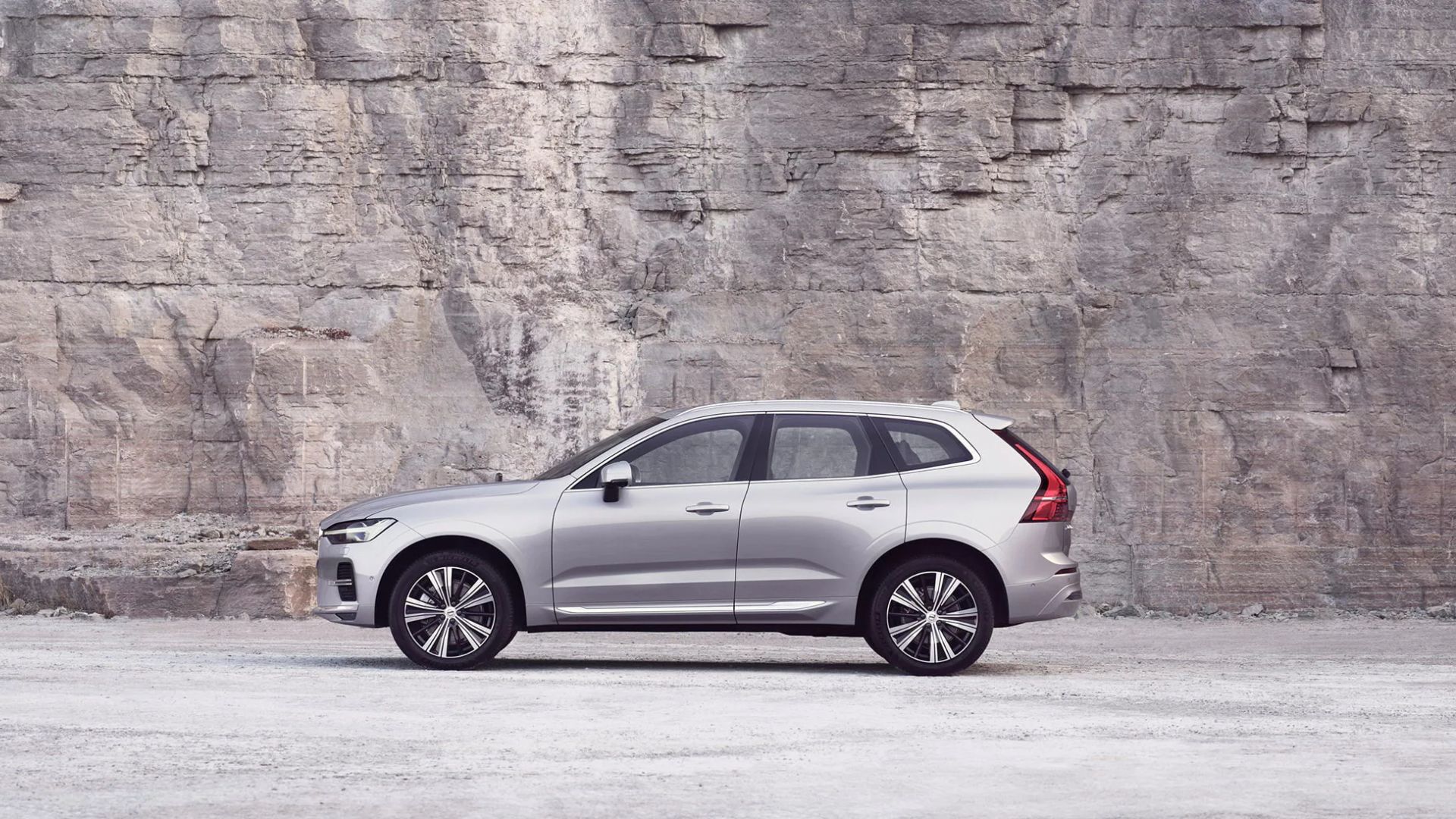 a silver volvo car parked in front of a stone wall.