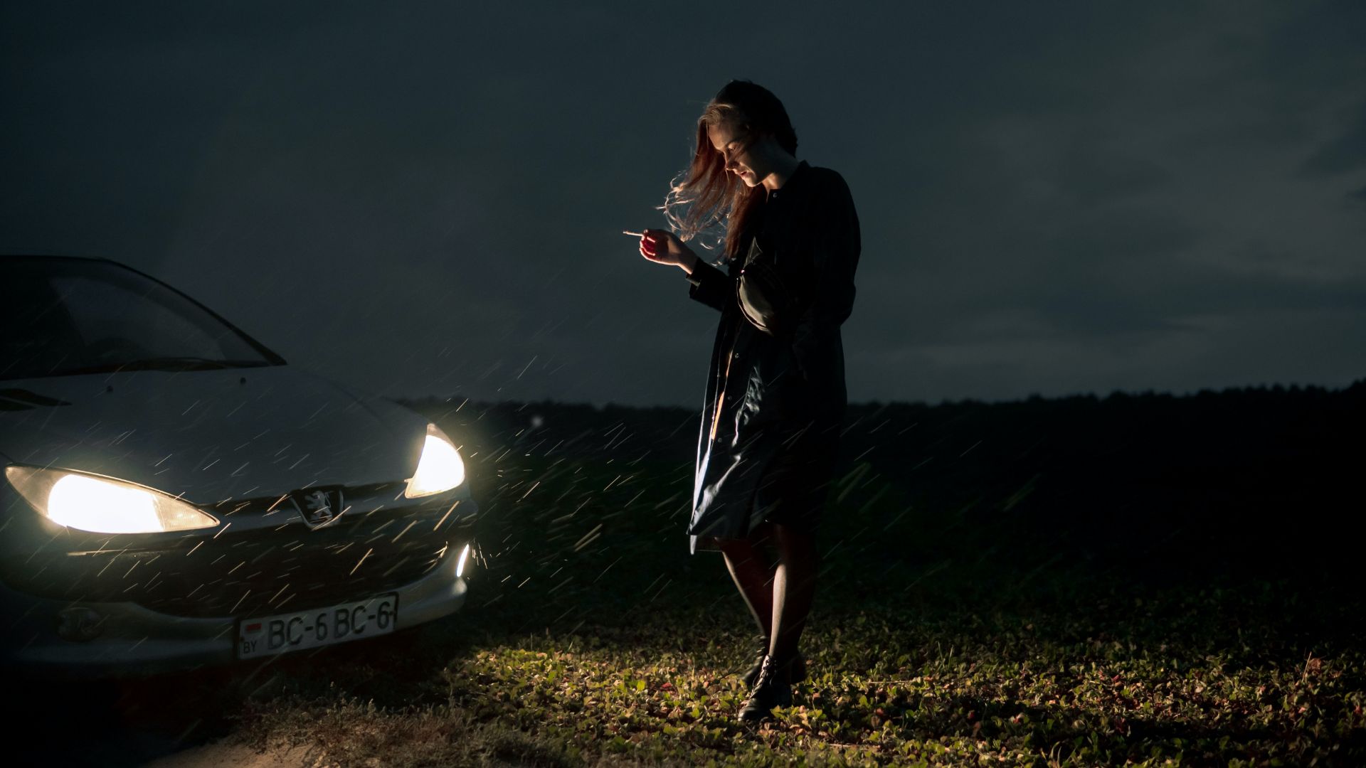 a woman standing next to a car in the rain.
